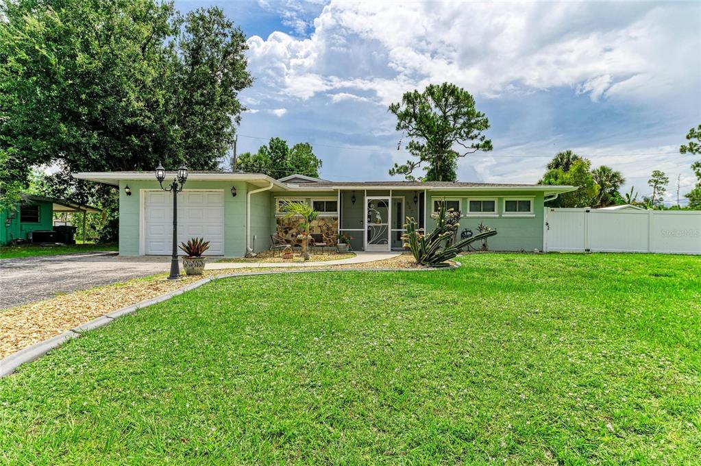 A single-story house with light green siding, a white garage door, and a grassy lawn — 557 READING STREET NW, PORT CHARLOTTE, FL
