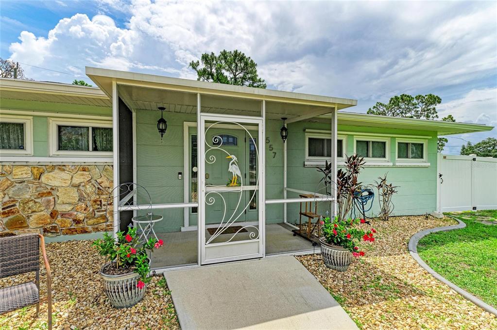 A light green house exterior features a screened front porch with a decorative heron door — 557 READING STREET NW, PORT CHARLOTTE, FL