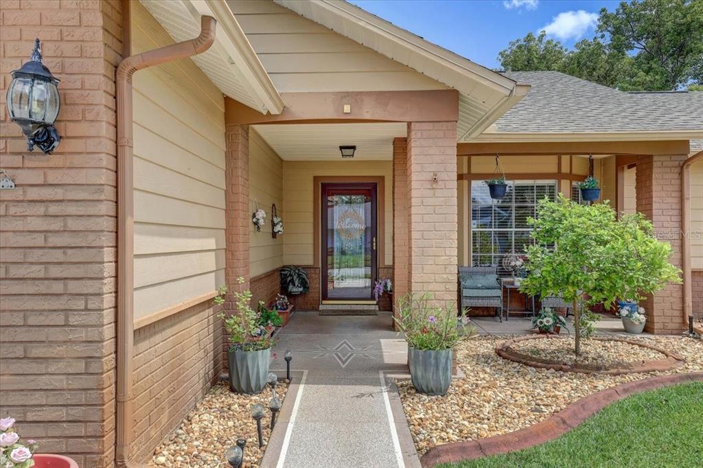 A covered front porch with a brick facade, a glass storm door, and potted plants — 9909 SAINT JOSEPH COURT, NEW PORT RICHEY, FL