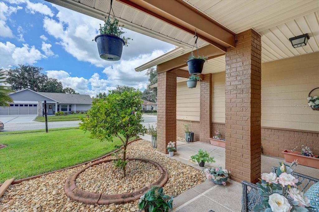 A covered front porch features brick columns, hanging planters, and a small tree in gravel — 9909 SAINT JOSEPH COURT, NEW PORT RICHEY, FL