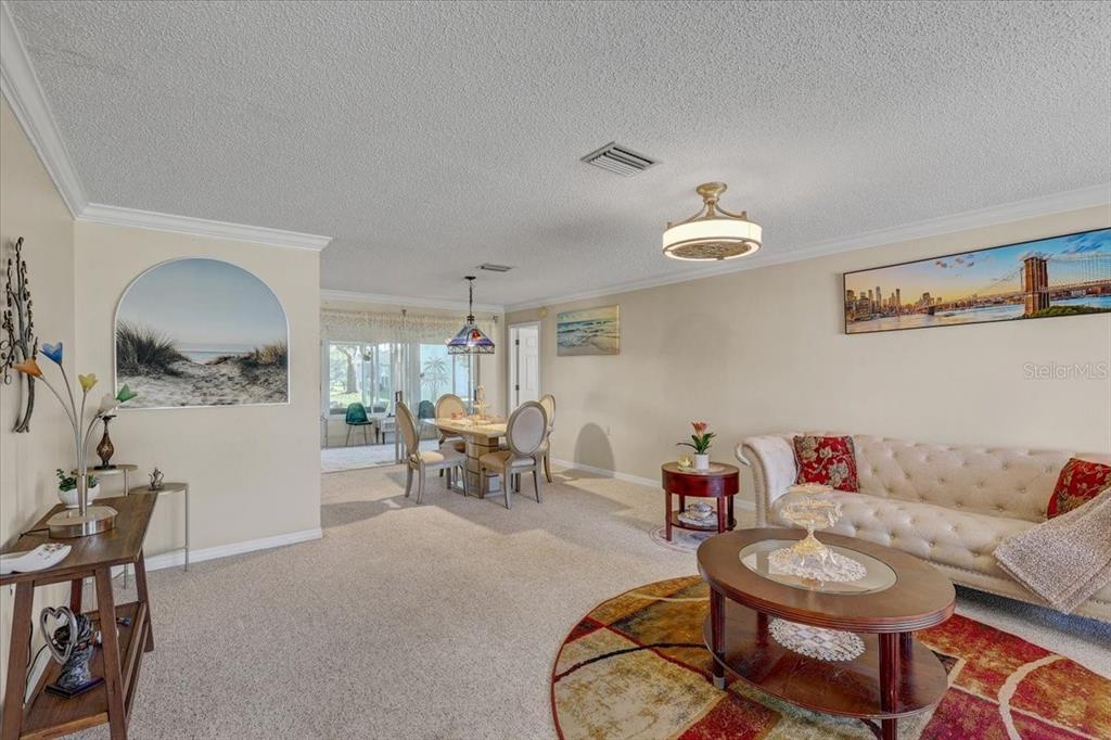 A living and dining area features beige carpeting, a tufted sofa, and a glass-topped table — 9909 SAINT JOSEPH COURT, NEW PORT RICHEY, FL