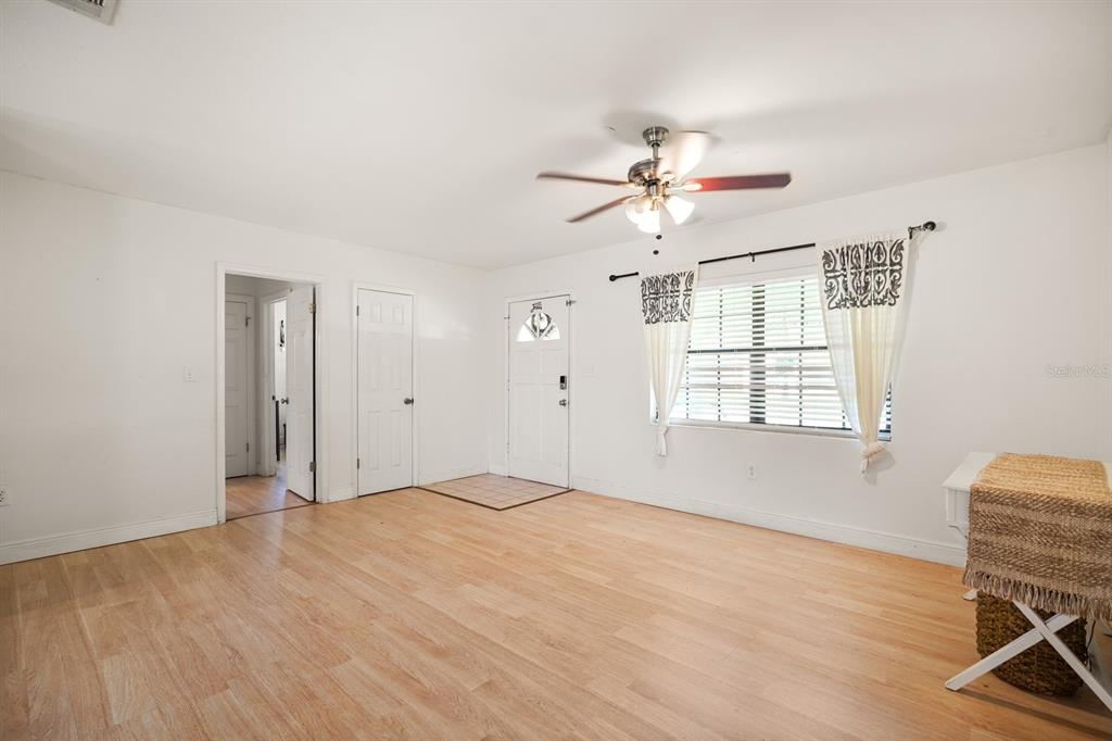 A living room with light wood-look flooring, a ceiling fan, and a white front door — 814 DENSMORE DR, WINTER PARK, FL