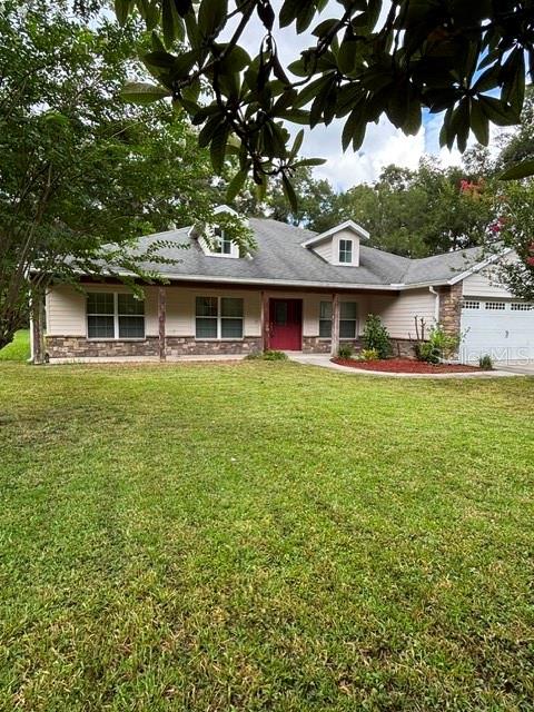 A single-story house with a light-colored exterior, a red front door, and a grassy lawn — 9209 MCINTYRE ROAD, BROOKSVILLE, FL