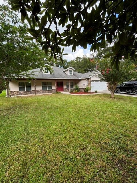 A single-story house with a light-colored exterior, a red front door, and a large lawn — 9209 MCINTYRE ROAD, BROOKSVILLE, FL