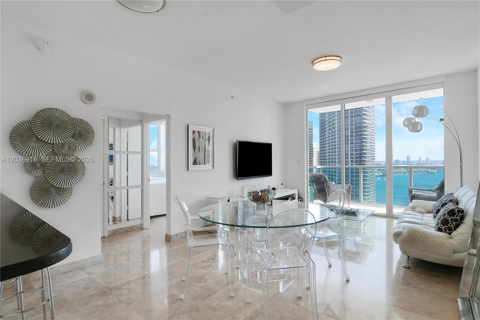 A bright living and dining area features glass furniture, marble floors, and a balcony view — 31 SE 5th St # 3812, Miami FL 33131, MIAMI, FL