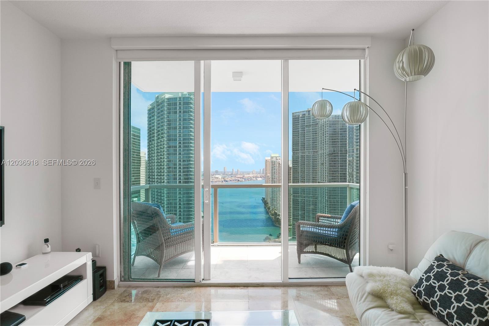 A living room with a sliding glass door opens to a balcony overlooking the water — 31 SE 5th St # 3812, Miami FL 33131, MIAMI, FL