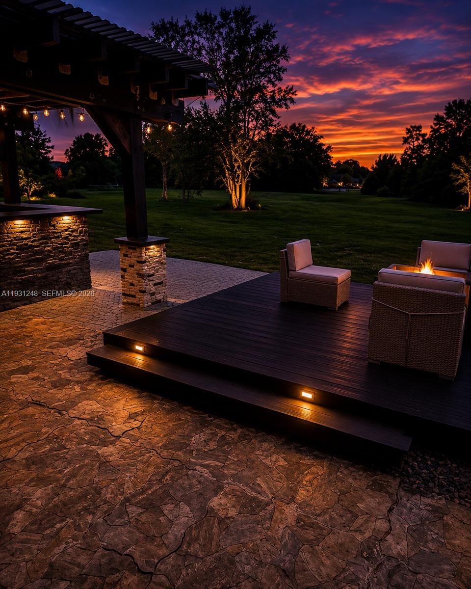 A stone patio with a dark wood deck, fire pit, and pergola at sunset — 4905 Banyan Lane, Tamarac FL 33319, TAMARAC, FL