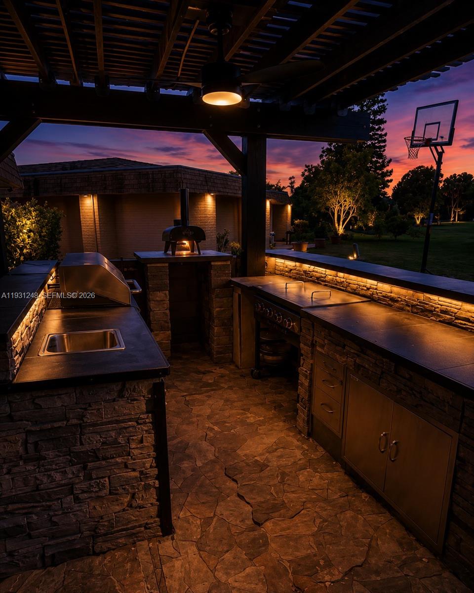 An outdoor kitchen features stone counters, a pizza oven, a grill, and a sink — 4905 Banyan Lane, Tamarac FL 33319, TAMARAC, FL