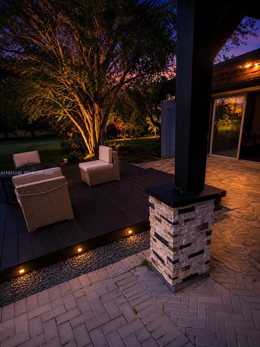 A patio features a stone-tiled floor, a raised dark wood deck, and outdoor seating at dusk — 4905 Banyan Lane, Tamarac FL 33319, TAMARAC, FL