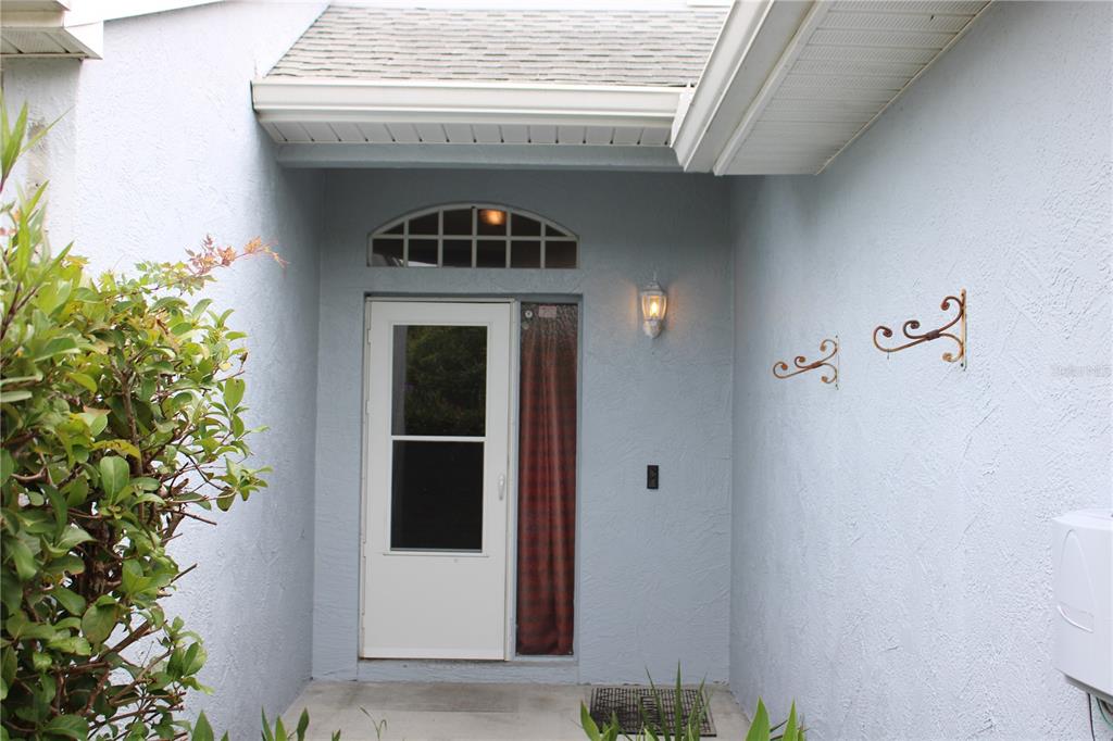 A light blue exterior entryway features a white storm door, a transom window, and wall-mounted decor — 202 HEMINGWAY DRIVE, OLDSMAR, FL