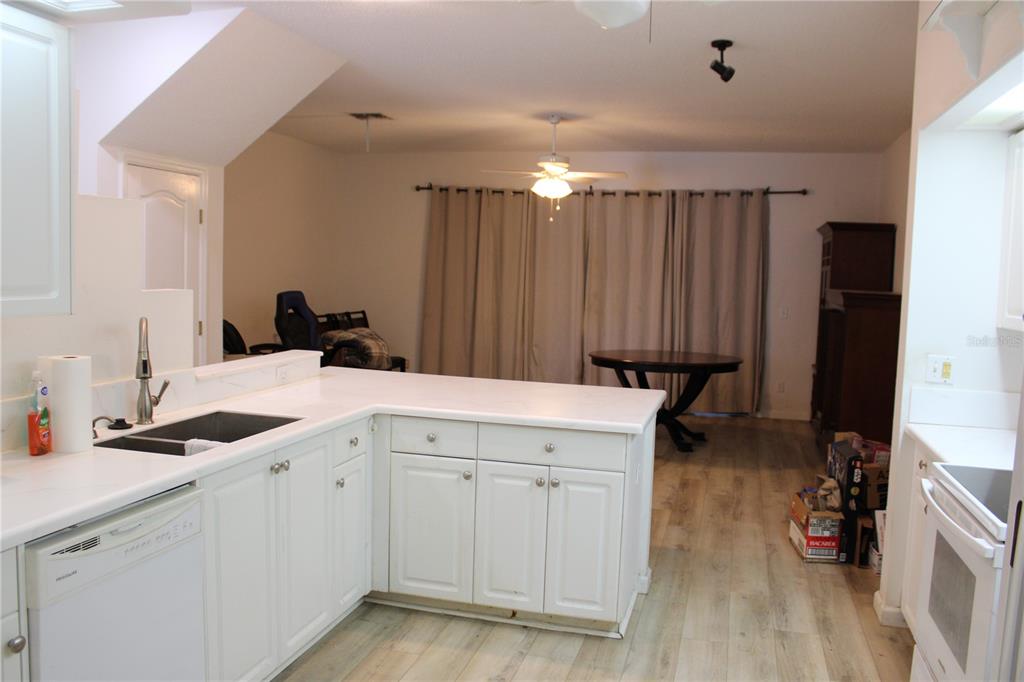 A white kitchen with a peninsula overlooks a dining area with wood-look flooring and curtains — 202 HEMINGWAY DRIVE, OLDSMAR, FL
