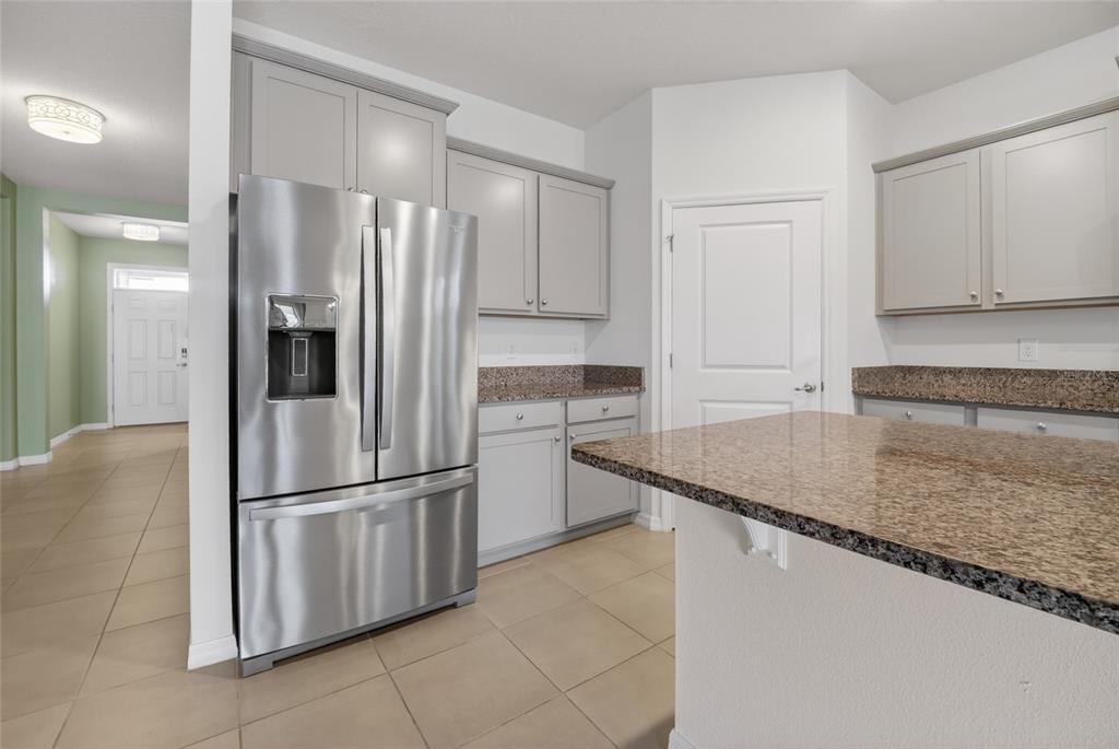 A kitchen features gray cabinetry, granite countertops, stainless steel appliances, and tile flooring — 8872 SW 63RD AVENUE, OCALA, FL