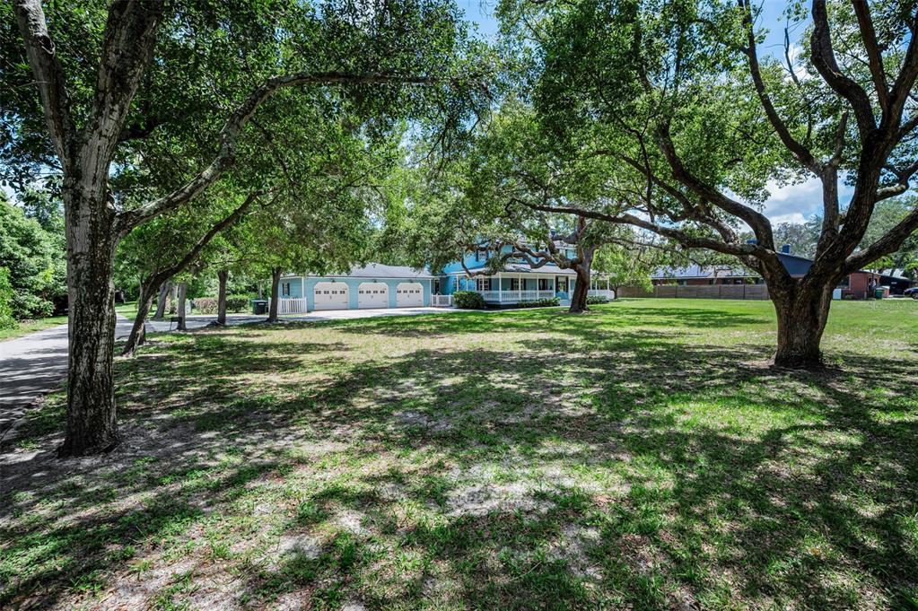 A light blue two-story house with a three-car garage sits behind large oak trees — 3525 FAIRVIEW STREET, SAFETY HARBOR, FL