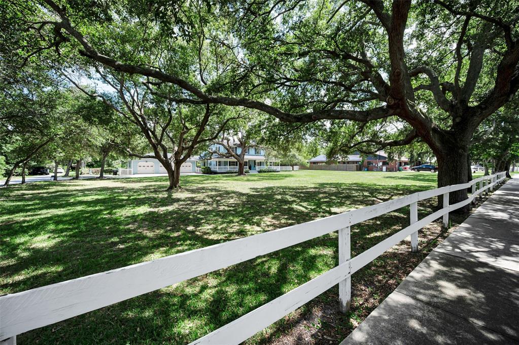 A white fence borders a large, grassy yard shaded by mature trees in front of houses — 3525 FAIRVIEW STREET, SAFETY HARBOR, FL