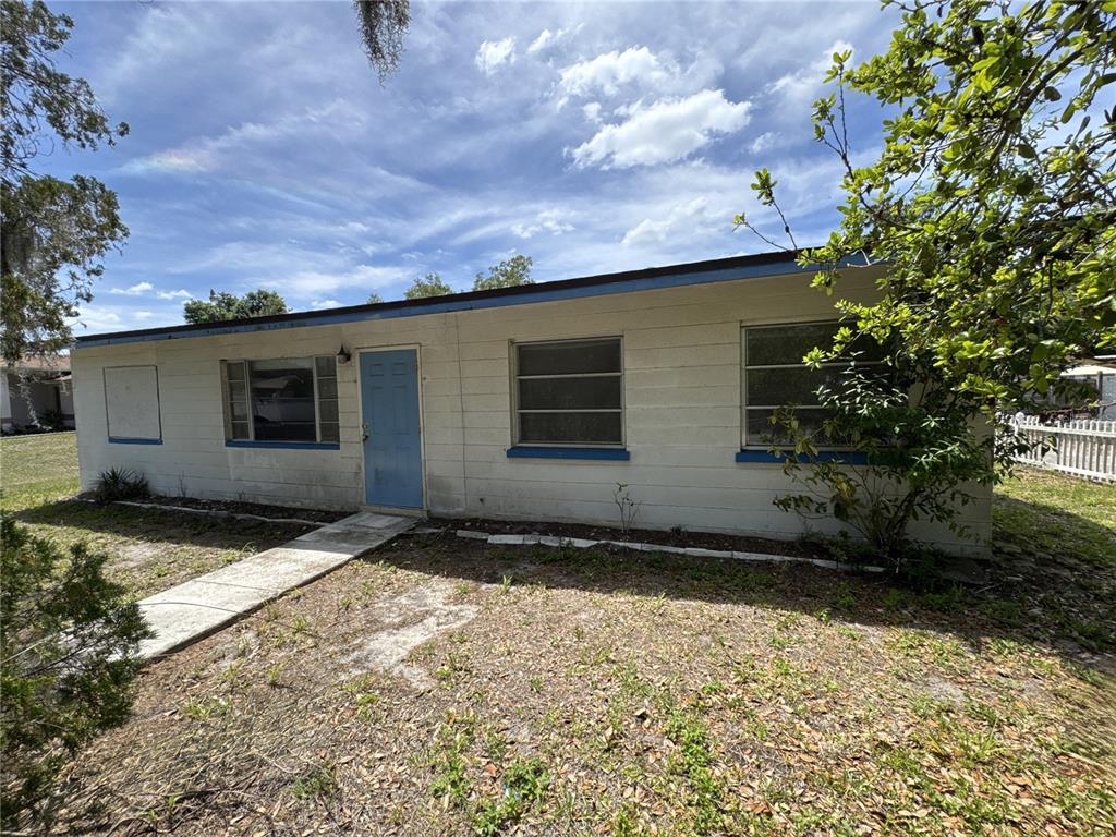 The exterior of a single-story house with white siding, a blue door, and metal-framed windows — 4103 BRAZILNUT AVENUE, SARASOTA, FL