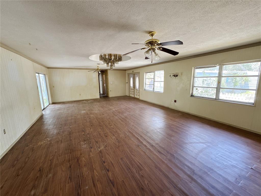A large, empty living room features wood-look flooring, paneled walls, and two ceiling fans — 4103 BRAZILNUT AVENUE, SARASOTA, FL