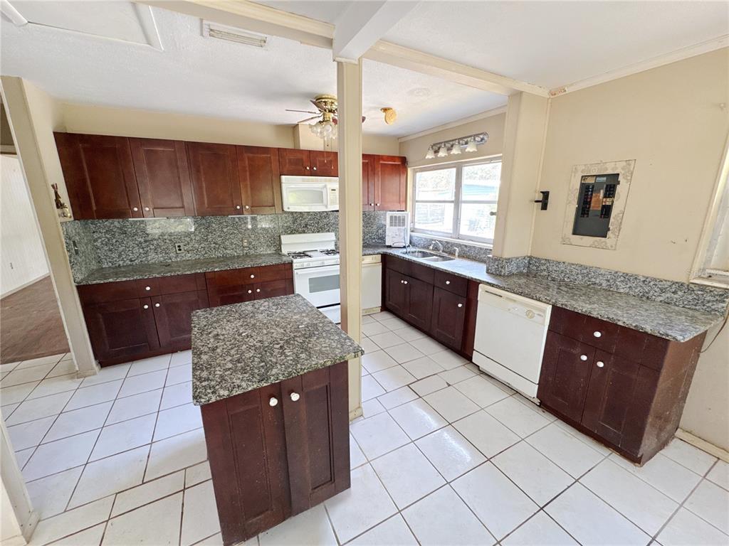 A kitchen features dark wood cabinets, granite countertops, a center island, and white tile flooring — 4103 BRAZILNUT AVENUE, SARASOTA, FL
