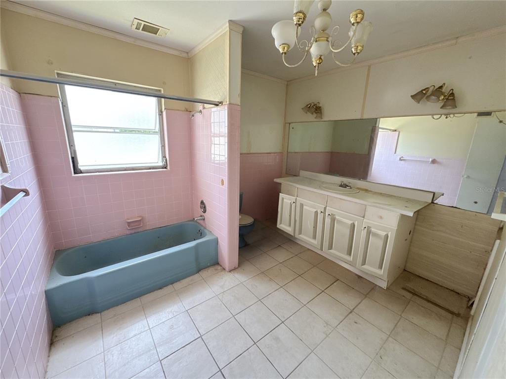 A bathroom features pink tiled walls, a blue bathtub, white cabinetry, and tile flooring — 4103 BRAZILNUT AVENUE, SARASOTA, FL