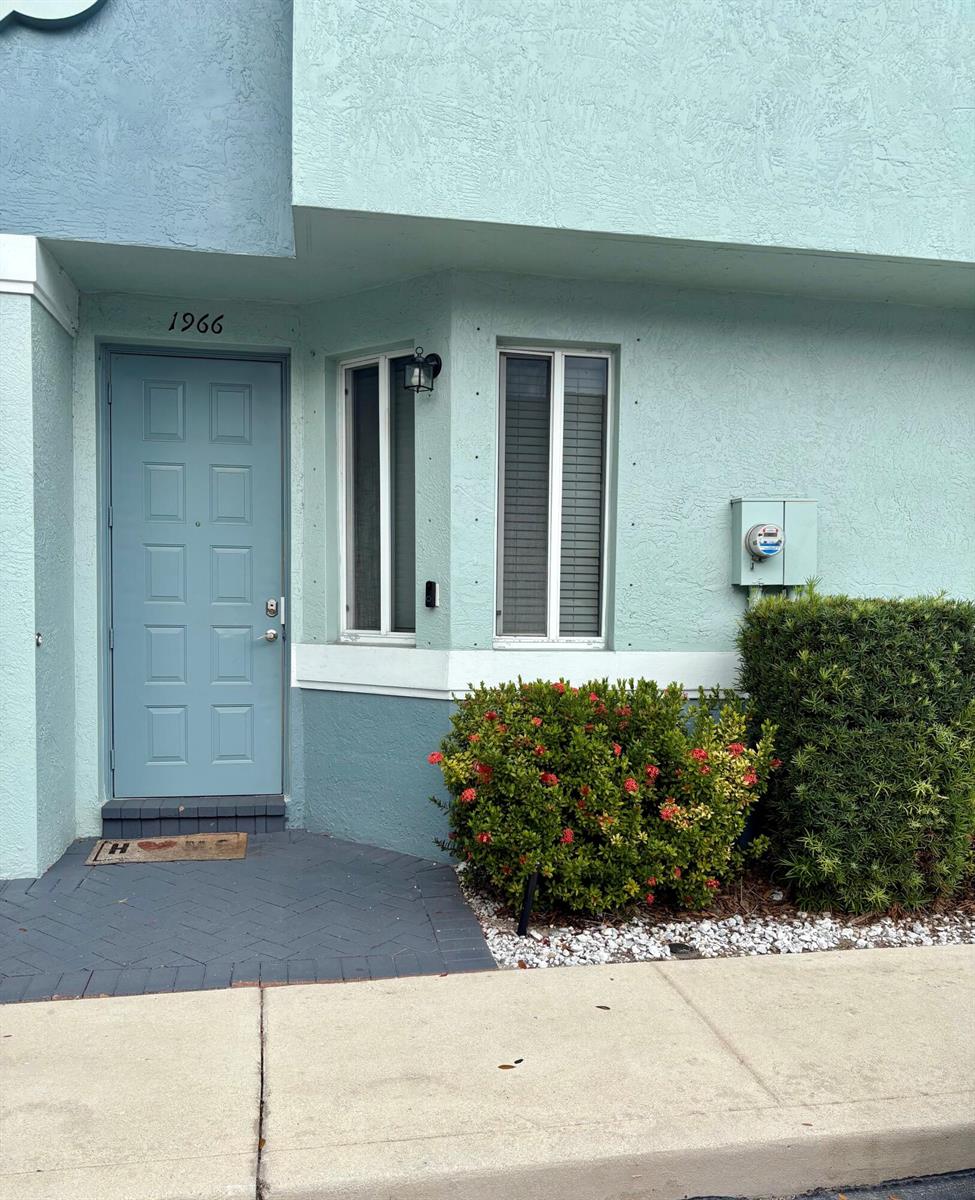 The exterior of a light blue building features a front door, windows, and landscaping — 1966 Alamanda Way, Riviera Beach FL 33404, RIVIERA BEACH, FL