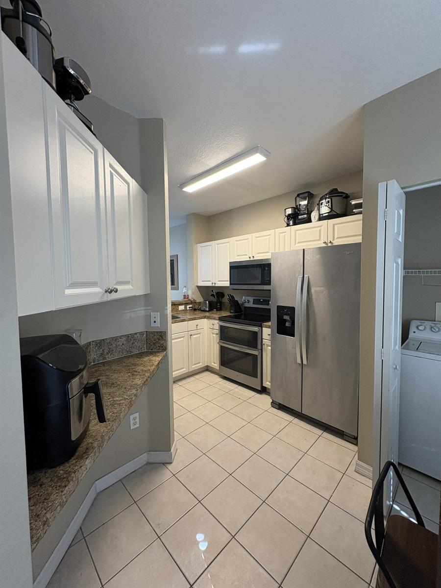 A kitchen features white cabinets, granite countertops, stainless steel appliances, and tile flooring — 1966 Alamanda Way, Riviera Beach FL 33404, RIVIERA BEACH, FL