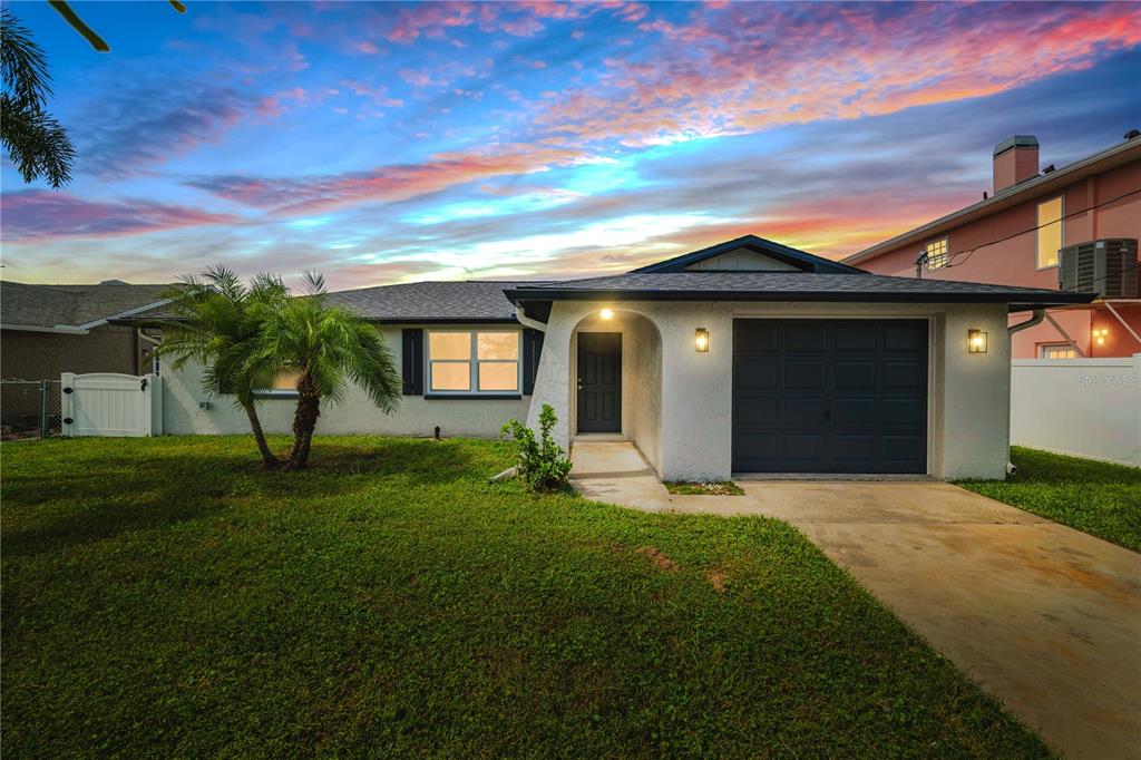 A single-story house with a gray garage, dark front door, and a palm tree — 6617 HARBOR DRIVE, HUDSON, FL