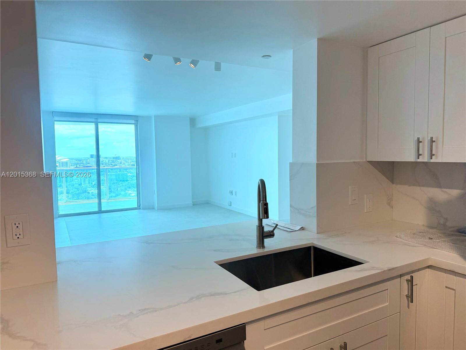 A kitchen sink and white marble-style countertop overlook a bright living area with balcony access — 2101 Brickell Ave # 2301, Miami FL 33129, MIAMI, FL