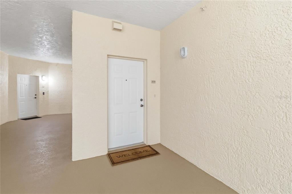 A white apartment door with a welcome mat in a beige, textured-wall hallway — 6336 BUFORD STREET UNIT 209, ORLANDO, FL