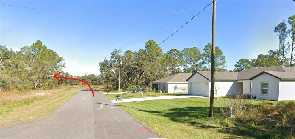A paved road leads toward a wooded area next to a modern suburban house — 364 BOWFIN DRIVE, POINCIANA, FL