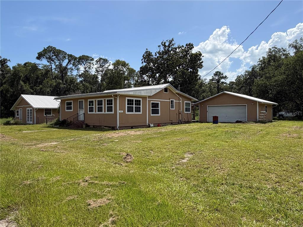A tan, single-story house with a detached garage sits on a large, grassy lot — 9929 FACTORY AVENUE, HAMPTON, FL