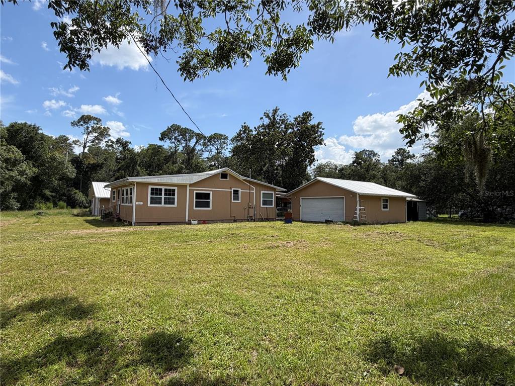 A tan single-story house with a detached garage sits on a large, grassy lot — 9929 FACTORY AVENUE, HAMPTON, FL