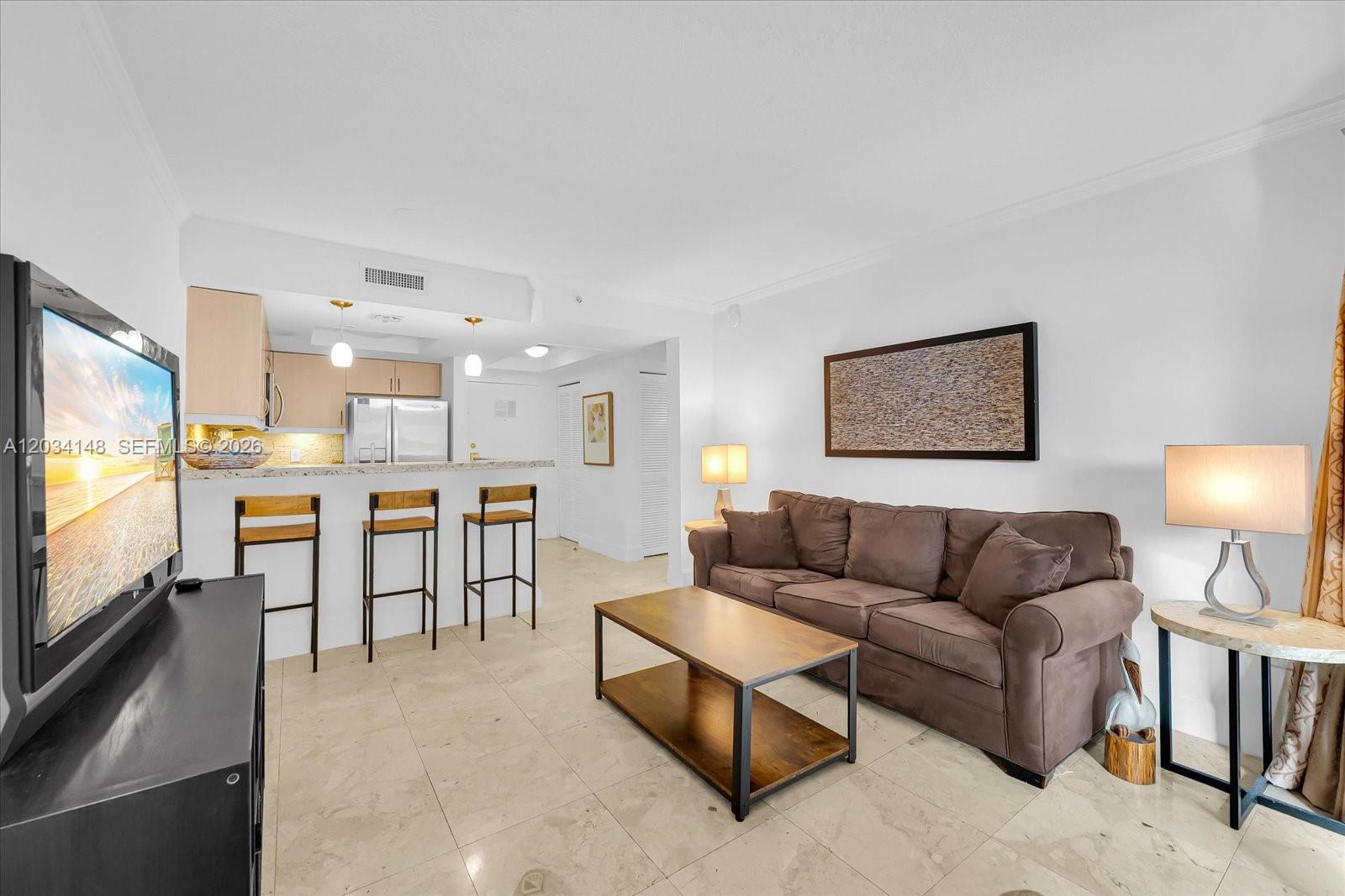 A living room with a brown sofa, coffee table, and an open kitchen with barstools — 2951 S Bayshore Dr # 307, Miami FL 33133, MIAMI, FL