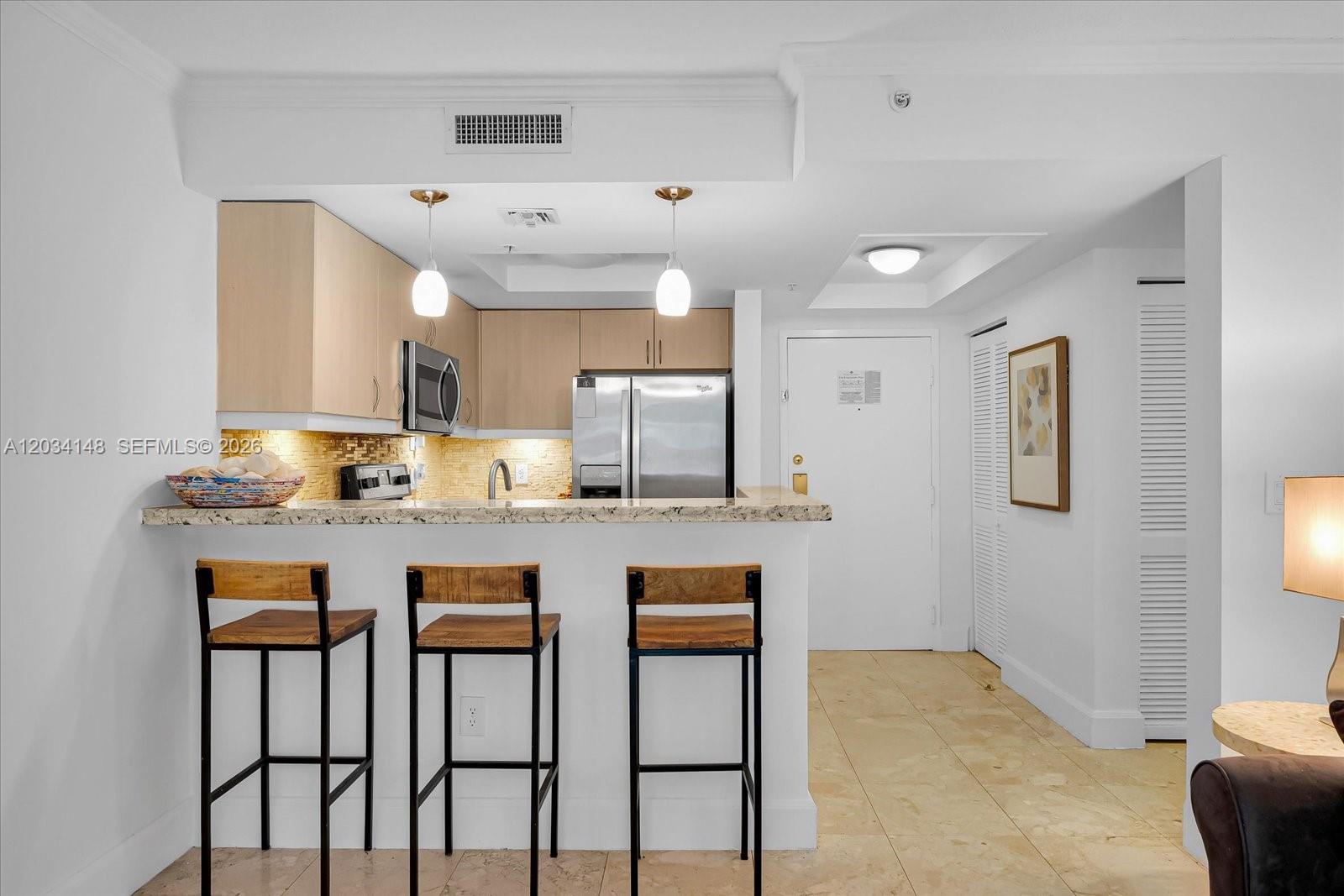 A kitchen features light wood cabinets, granite countertops, and a breakfast bar with three stools — 2951 S Bayshore Dr # 307, Miami FL 33133, MIAMI, FL