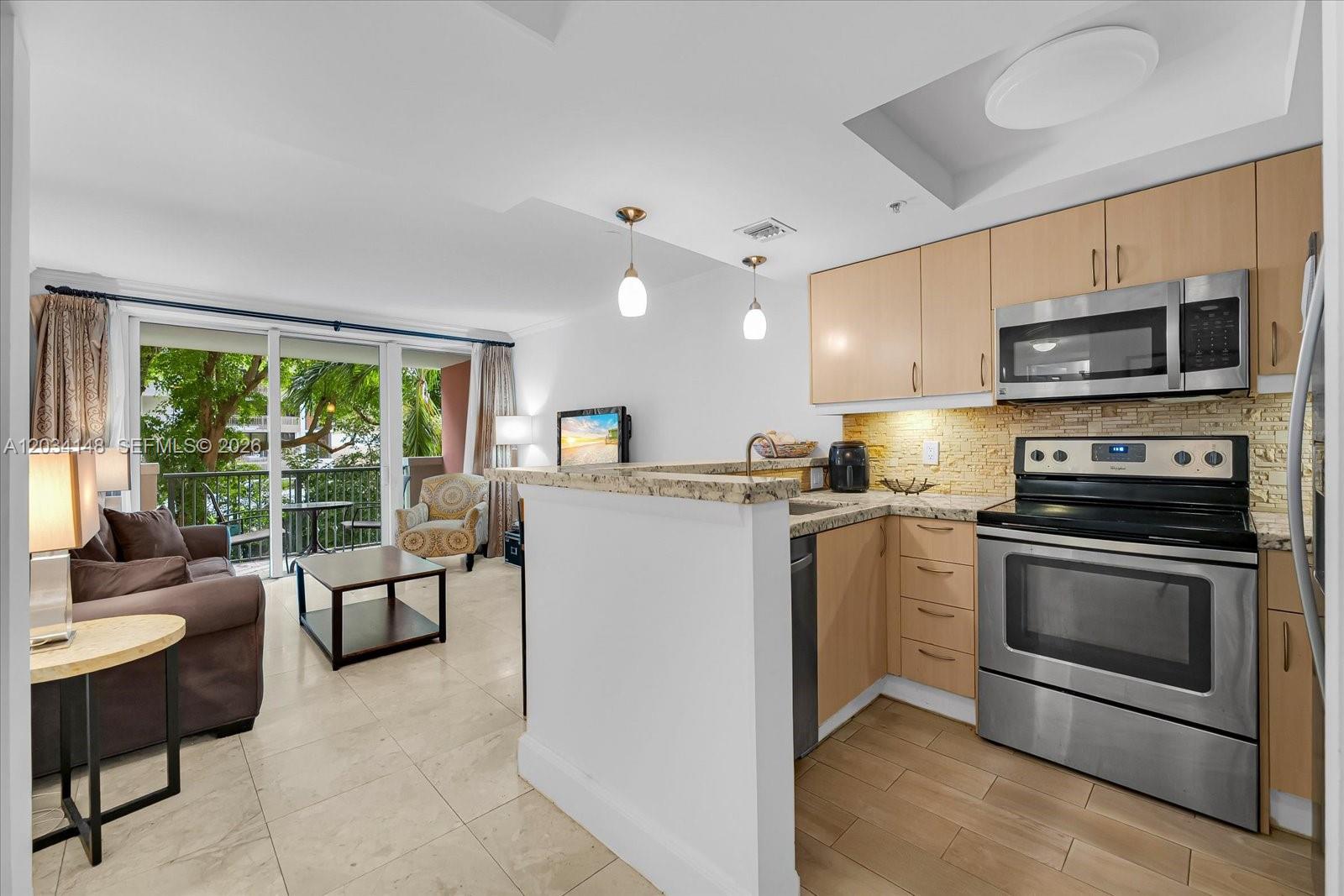 A kitchen with light wood cabinets and stainless steel appliances opens to a living area — 2951 S Bayshore Dr # 307, Miami FL 33133, MIAMI, FL