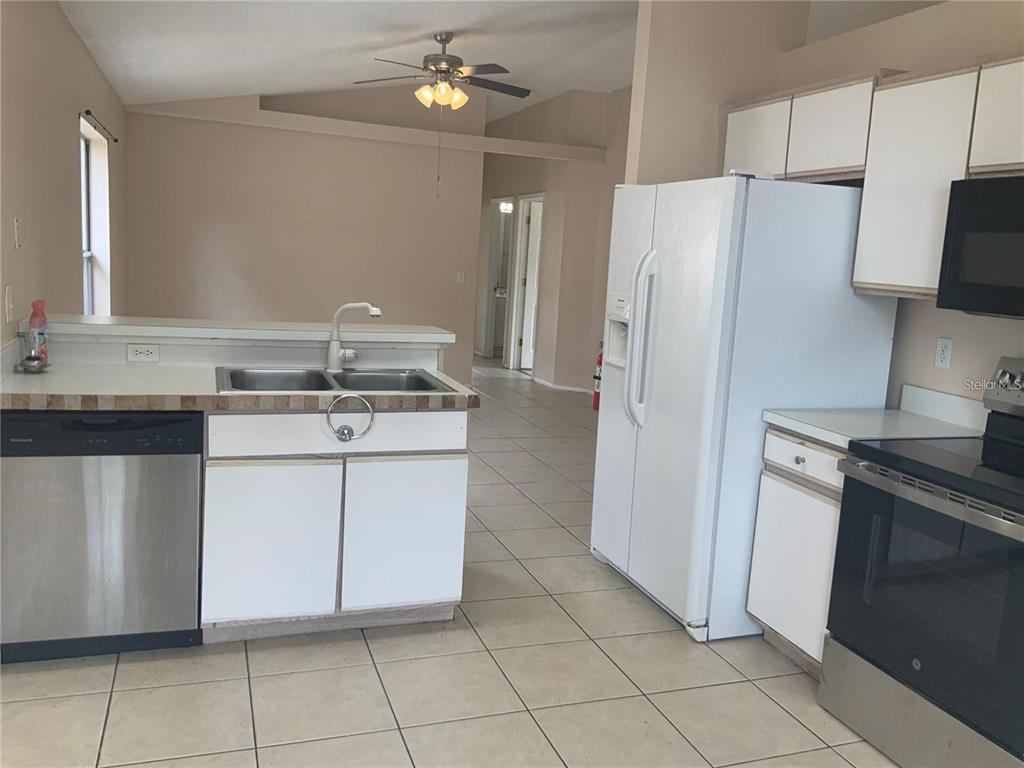 A kitchen features white cabinets, a stainless steel dishwasher, a white refrigerator, and tiled floors — 1705 CHATHAM CIRCLE, APOPKA, FL