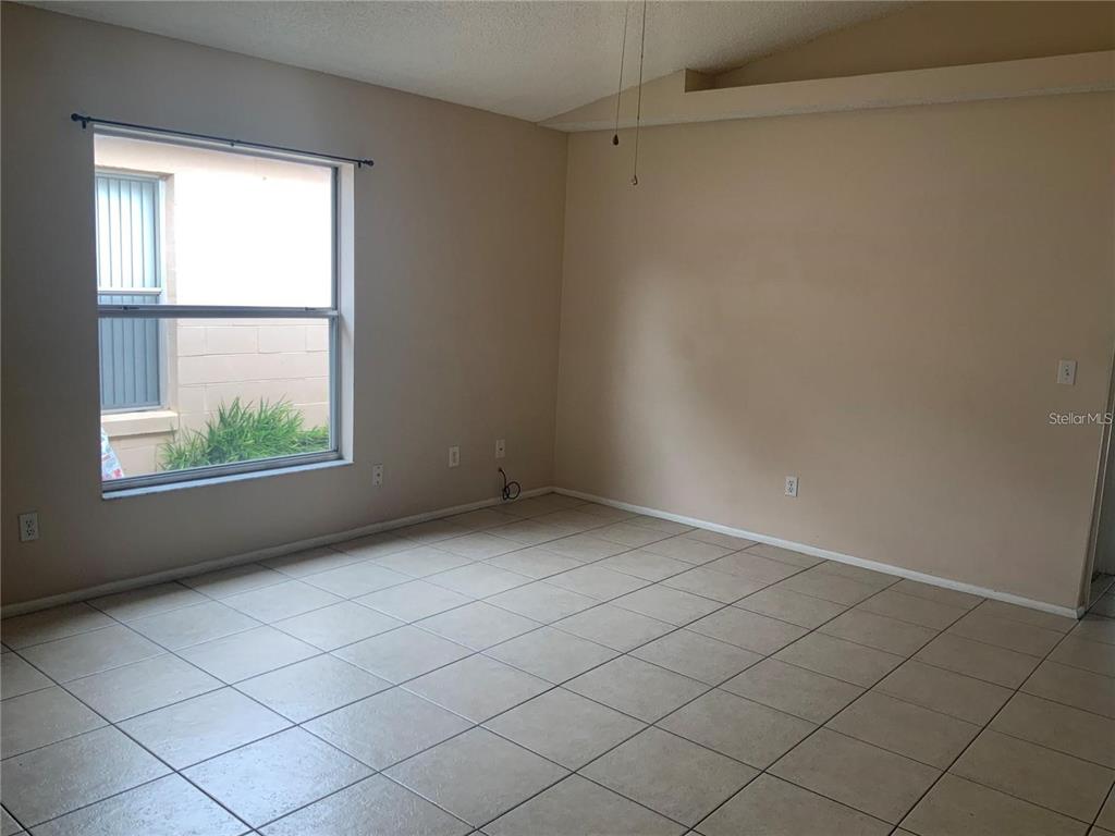 An empty room features beige walls, light-colored floor tiles, and a window overlooking a courtyard — 1705 CHATHAM CIRCLE, APOPKA, FL