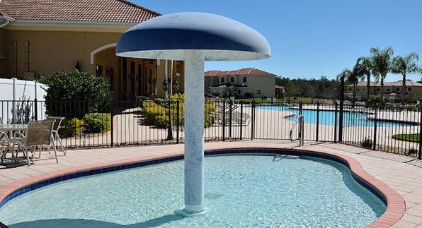A small circular pool with a mushroom-shaped water feature sits on a paved patio area — 1187 CHERVIL DRIVE, POINCIANA, FL