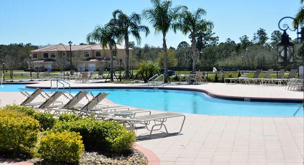 A swimming pool with lounge chairs on a patio surrounded by palm trees and buildings — 1187 CHERVIL DRIVE, POINCIANA, FL
