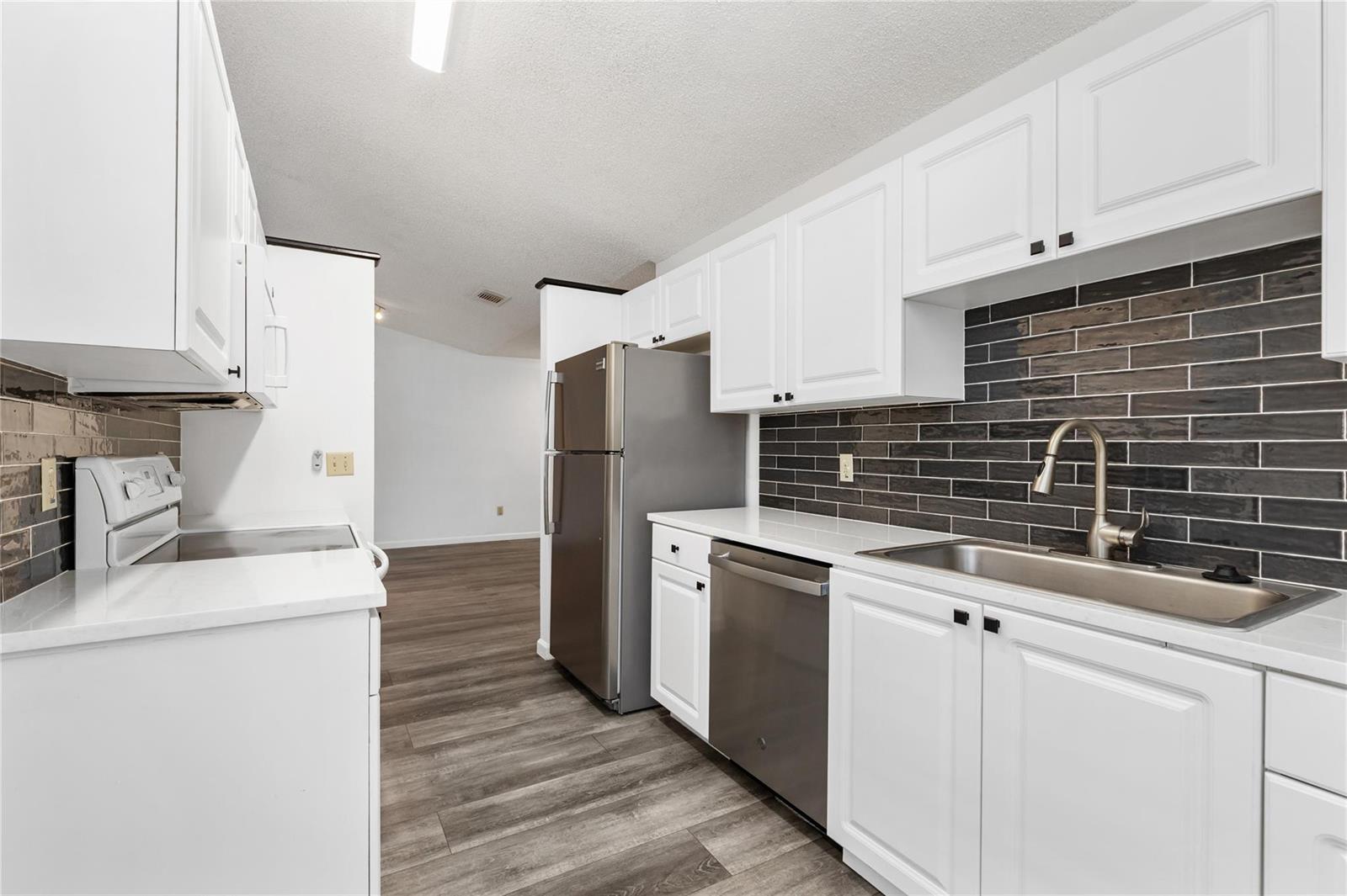 A kitchen features white cabinets, stainless steel appliances, and a dark horizontal tile backsplash — 9114 SW 20th Street # B, Boca Raton FL 33428, BOCA RATON, FL