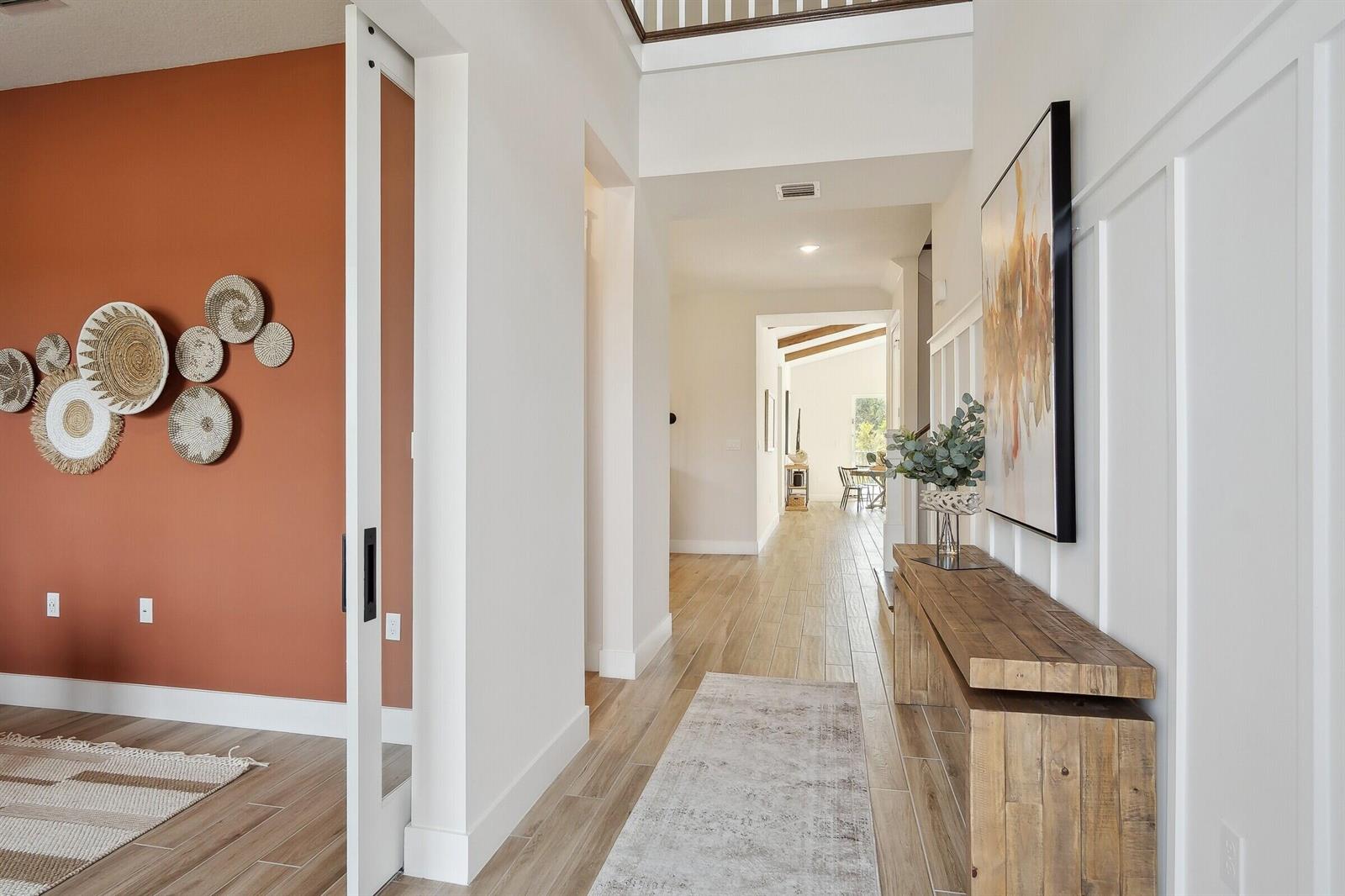 A hallway with wood-look tile floors leads toward a bright room with exposed ceiling beams — 6806 SE Lost Pine Drive, Stuart FL 34997, STUART, FL