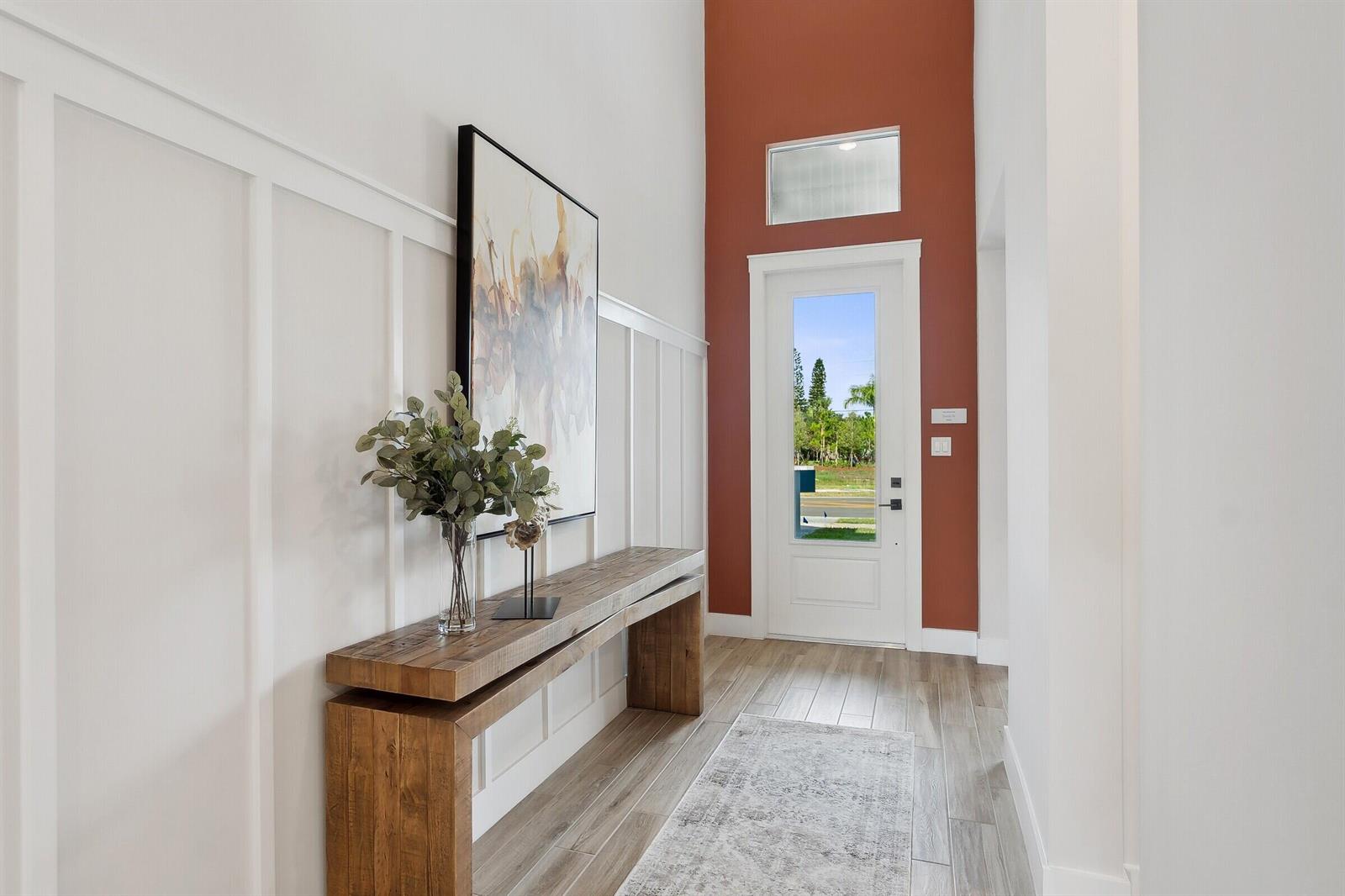 A modern entryway features a wooden console table, board and batten walls, and a red accent — 6806 SE Lost Pine Drive, Stuart FL 34997, STUART, FL