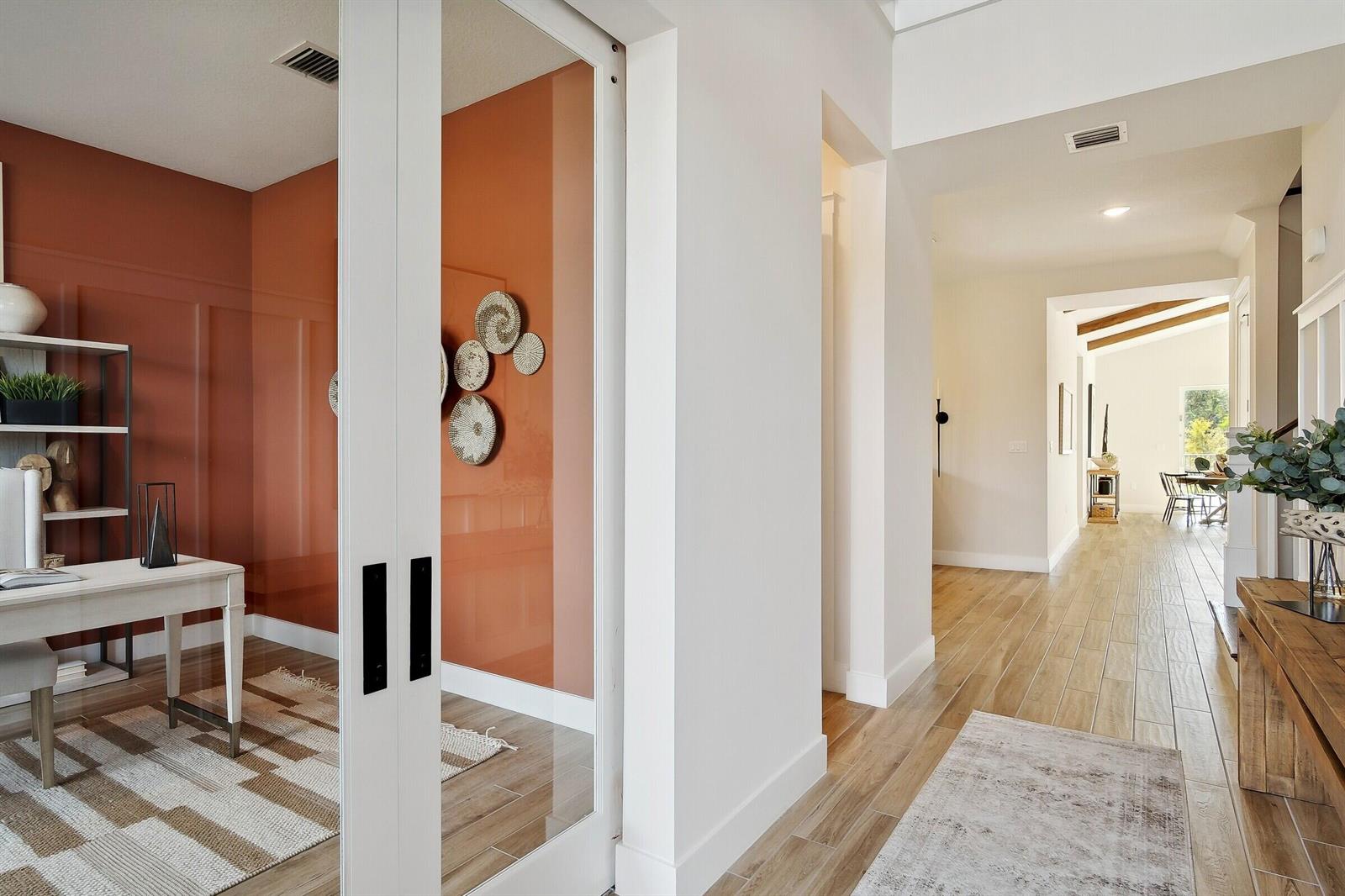A home office with terracotta walls and glass doors opens into a bright hallway — 6806 SE Lost Pine Drive, Stuart FL 34997, STUART, FL