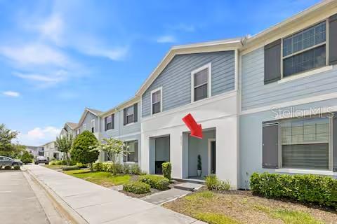 A red arrow points to the front entrance of a multi-story light blue townhouse — 8923 SYDNEY AVENUE, KISSIMMEE, FL