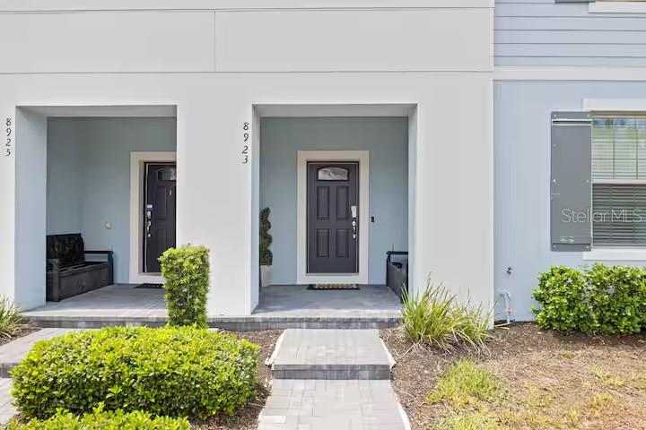 The exterior of two adjacent townhomes features light blue walls, dark doors, and paved entryways — 8923 SYDNEY AVENUE, KISSIMMEE, FL