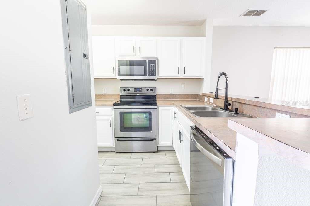 A kitchen features white cabinets, stainless steel appliances, a double sink, and light tile flooring — 141 JONES LANE UNIT A, KISSIMMEE, FL