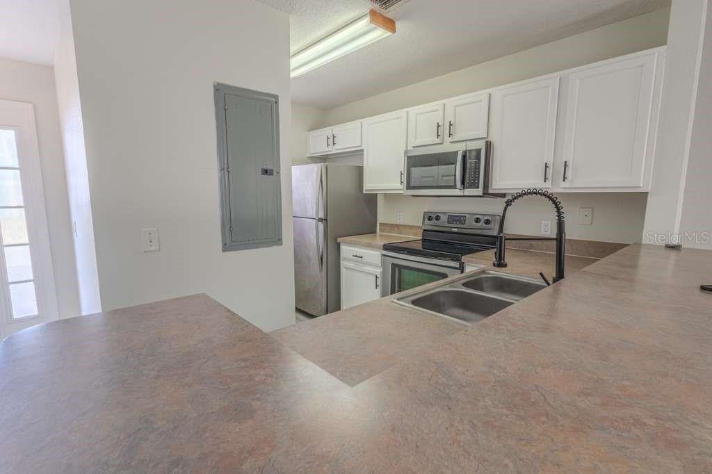 A kitchen features white cabinets, stainless steel appliances, and a brown laminate countertop — 141 JONES LANE UNIT A, KISSIMMEE, FL