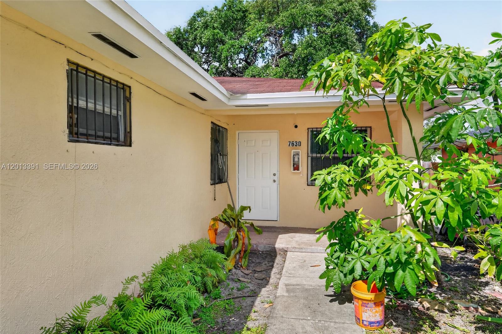 The exterior of a beige house features a white front door and security bars — 7628 NW 2nd Ct, Miami FL 33150, MIAMI, FL