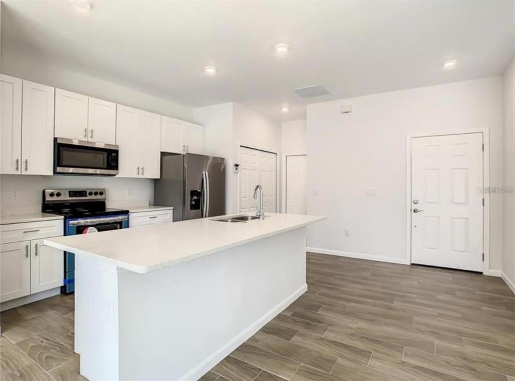 A modern kitchen features white cabinets, stainless steel appliances, a quartz island, and wood-look flooring — 17000 SW 41ST COURT, OCALA, FL