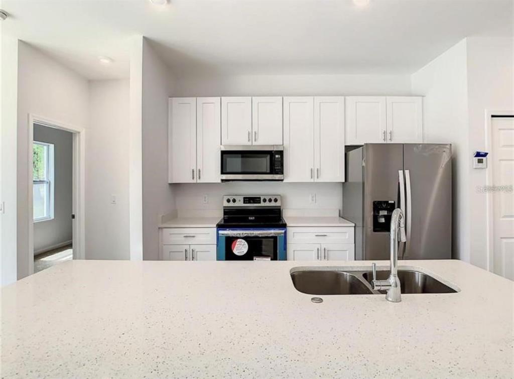 A kitchen features white cabinets, stainless steel appliances, and a quartz-topped island with a sink — 17000 SW 41ST COURT, OCALA, FL