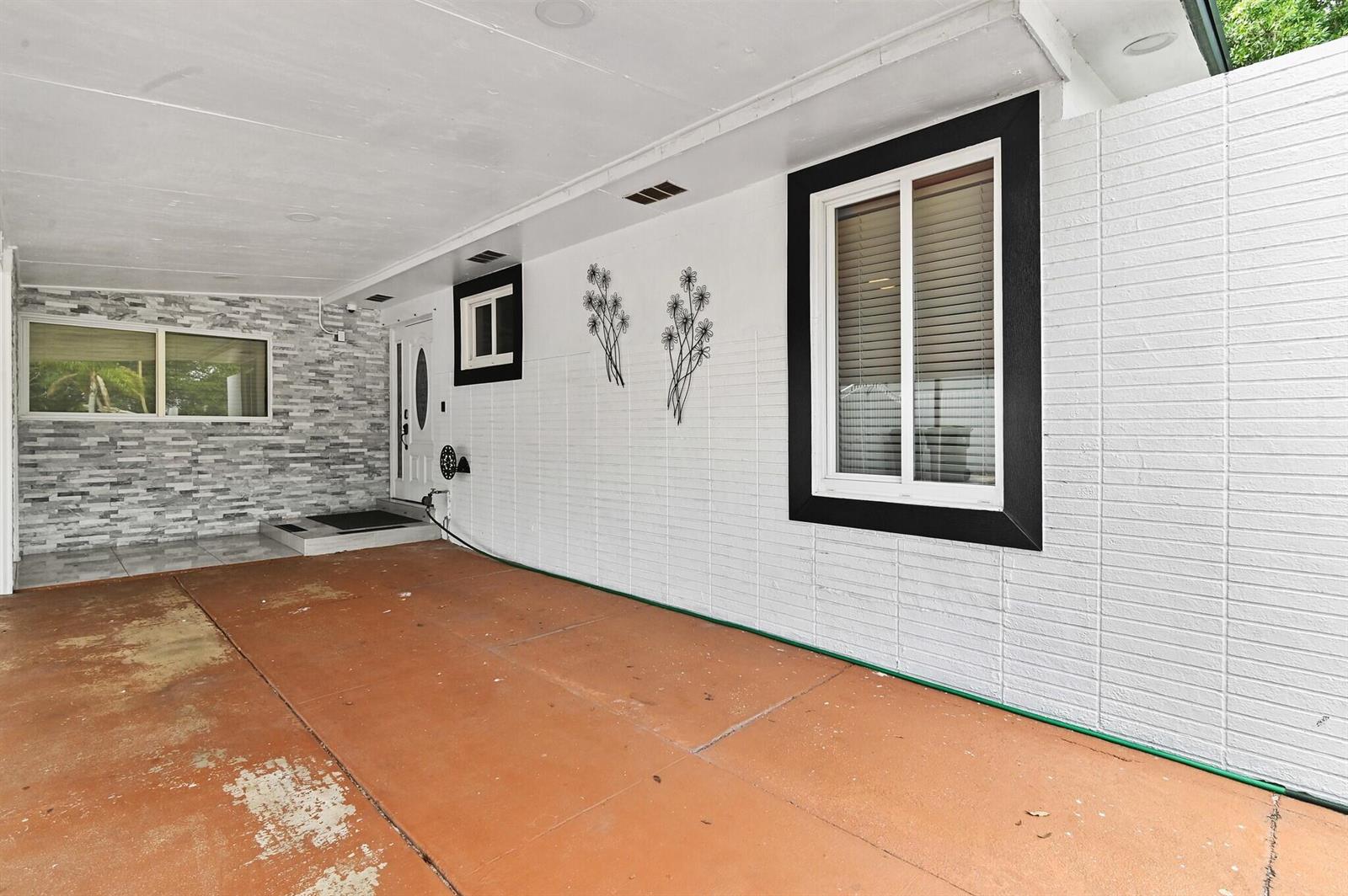 A covered carport area features a white brick wall, a window with black trim, and a door — 124 Davis Road, Palm Springs FL 33461, PALM SPRINGS, FL