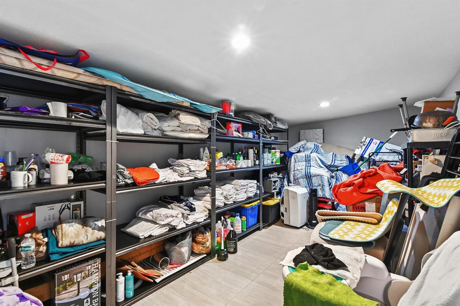 A storage room features metal shelving units filled with linens, household items, and miscellaneous supplies — 124 Davis Road, Palm Springs FL 33461, PALM SPRINGS, FL